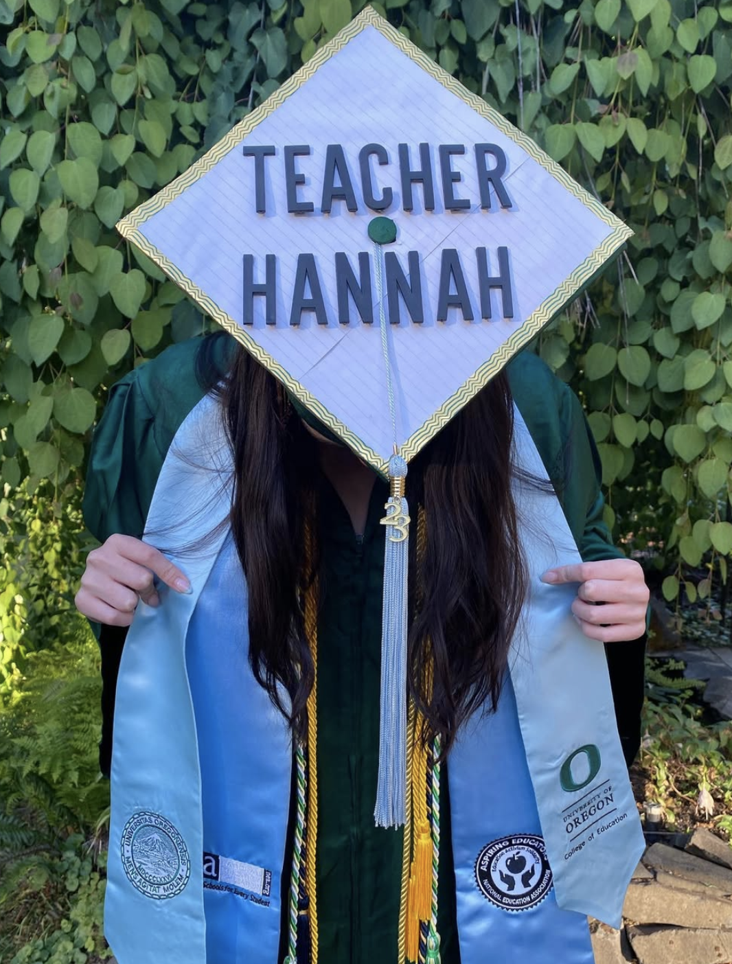 Hannah in a graduation cap and gown, smiling and holding her diploma.