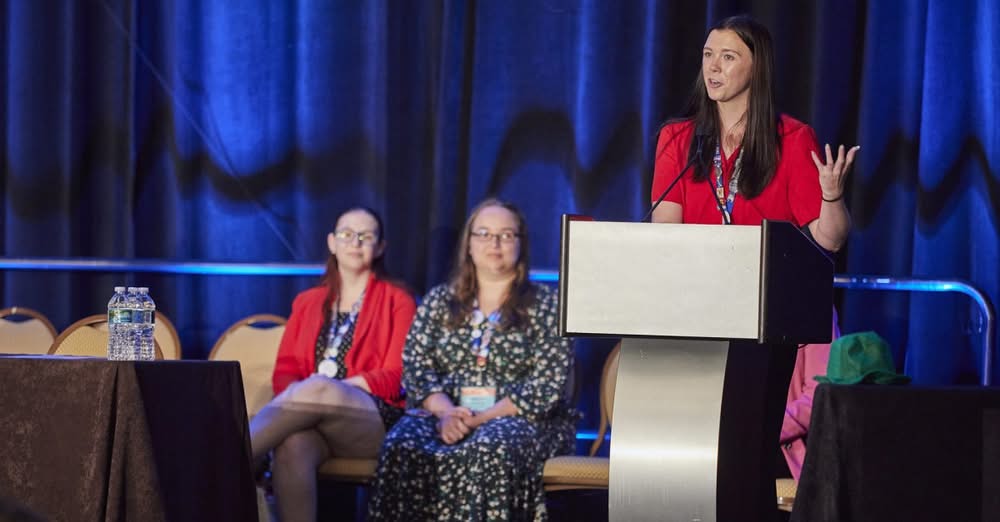 Hannah Speaking at a NEA Conference wearing a red button up. 